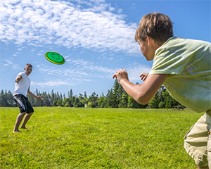 two boys playing frisbee in a field blue sky with cloud trails